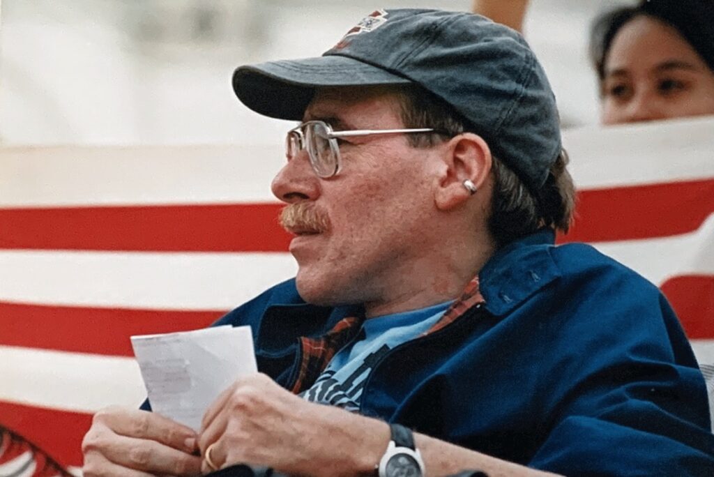 Paul Spooner looks to his right with the US Capitol Building and an American Flag serving as a backdrop.
